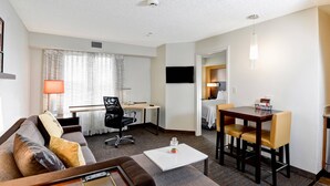 A hotel room with a sofa, a desk, a dining table with chairs, a TV mounted on the wall, and a lamp. - Residence Inn by Marriott Los Angeles LAX/El Segundo (El Segundo)
