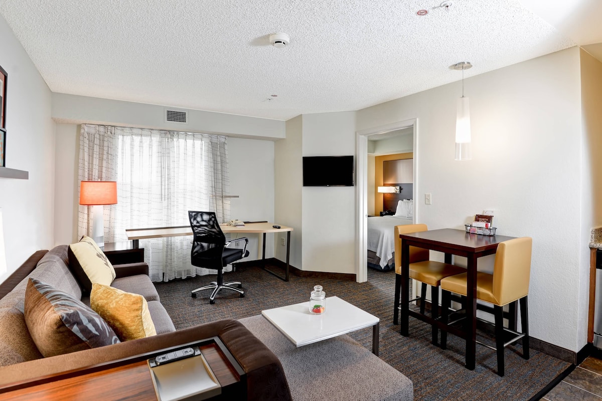Une chambre d’hôtel équipée d’un canapé, d’un bureau, d’une table à manger avec des chaises, d’un téléviseur fixé au mur et d’une lampe.
