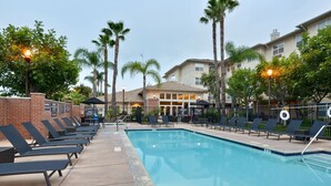 A swimming pool with lounge chairs and a brick wall, surrounded by palm trees and a building with a beige facade. - Residence Inn by Marriott Los Angeles LAX/El Segundo (El Segundo)