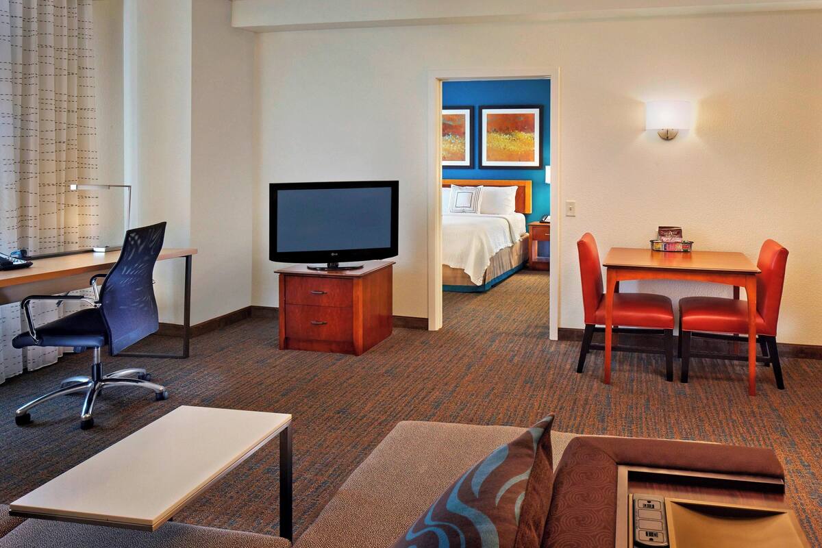 A hotel room with a desk, television, and a bed with a blue headboard.