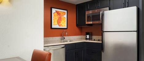 A compact kitchen with dark cabinets, a stainless steel refrigerator, a microwave, and a dishwasher.