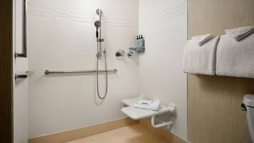 A bathroom with white tiled walls, a shower with a handheld showerhead, a toilet, and a towel rack with folded towels.
