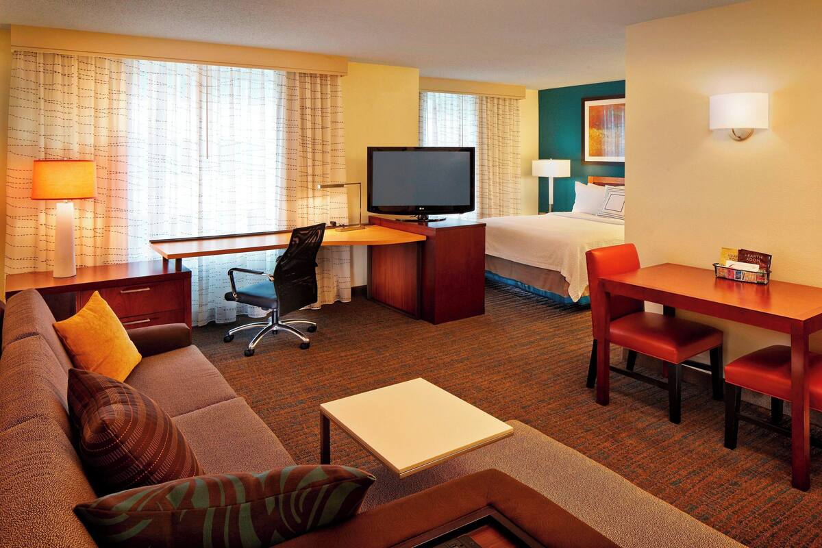 A hotel room with a bed, a desk with a television, a sofa, a small table, and a chair.