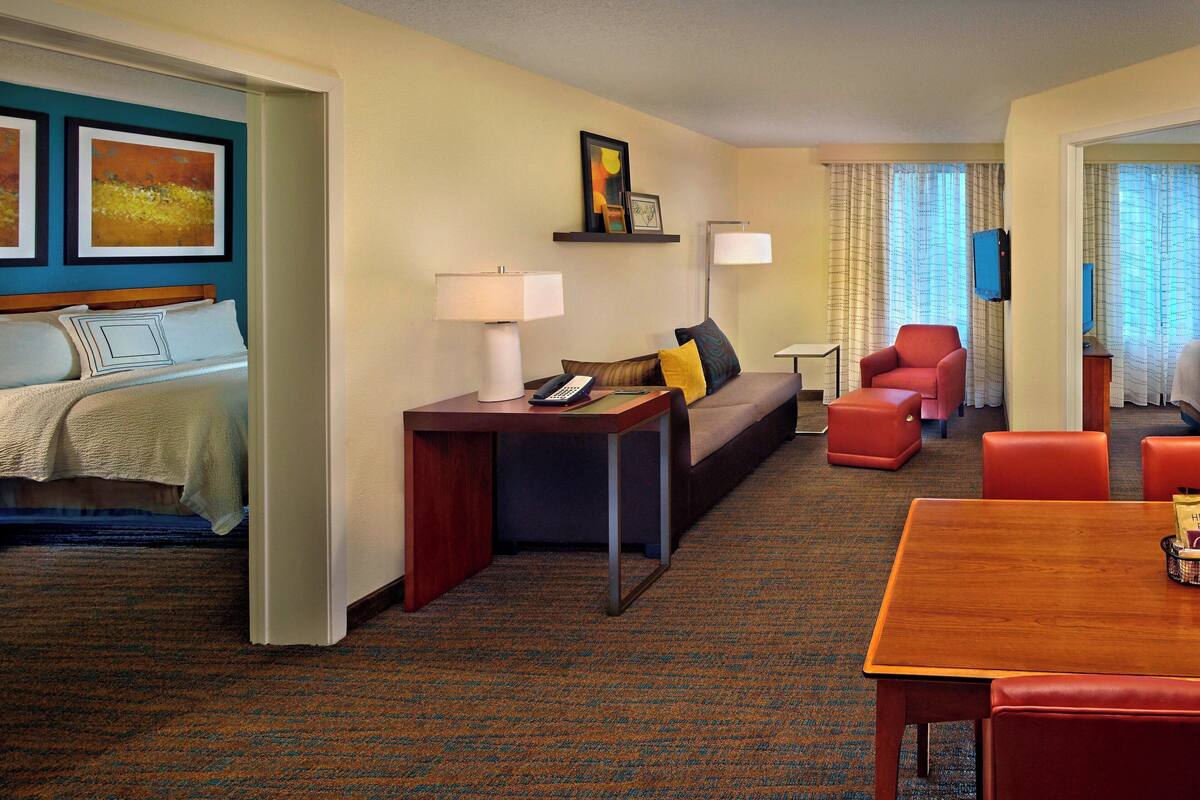 A hotel room with a bed, a sofa, a dining table, and a TV.