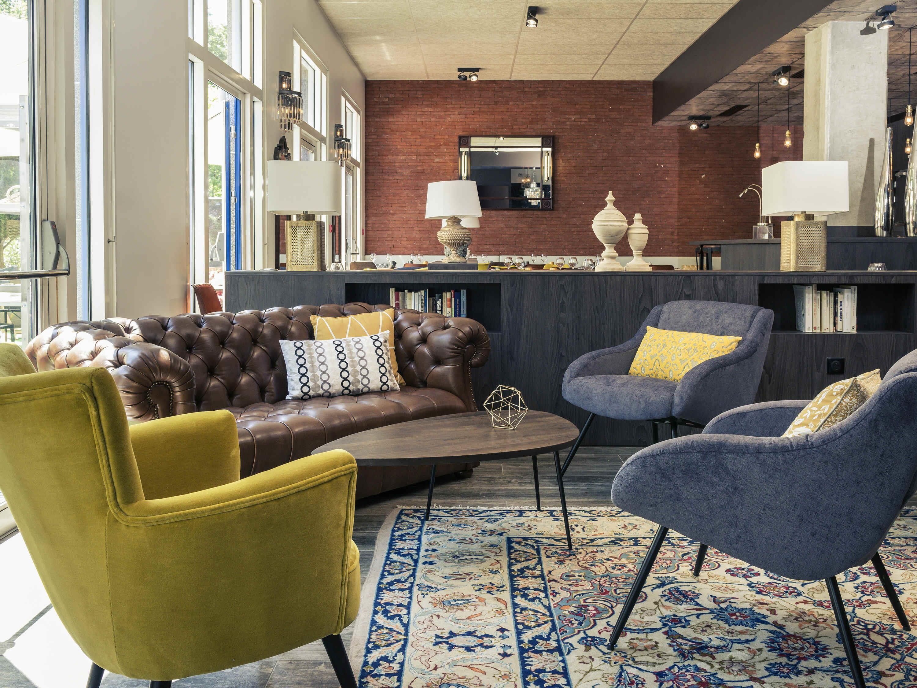 A modern living room with a leather sofa, a yellow armchair, and a blue armchair. There is a patterned rug on the floor.