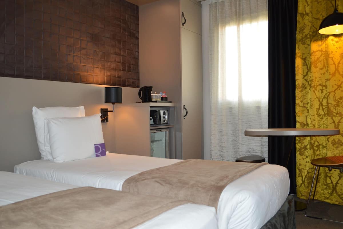 A hotel room with two beds, a minibar, a coffee machine, a small table, and a lamp.