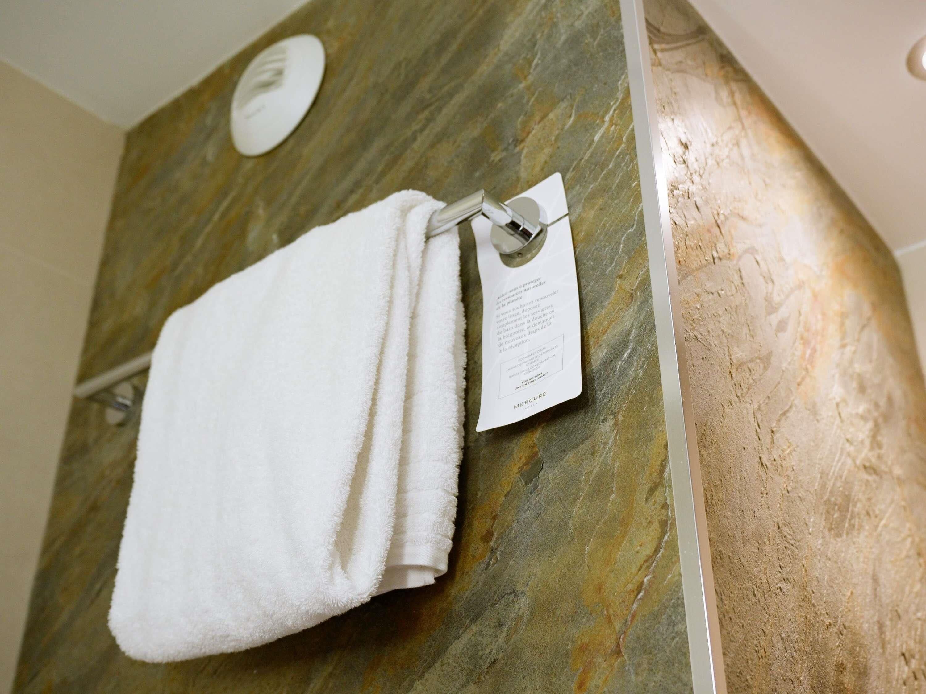 Une serviette blanche est suspendue à un porte-serviettes en métal dans une salle de bain dont le mur est recouvert de marbre.