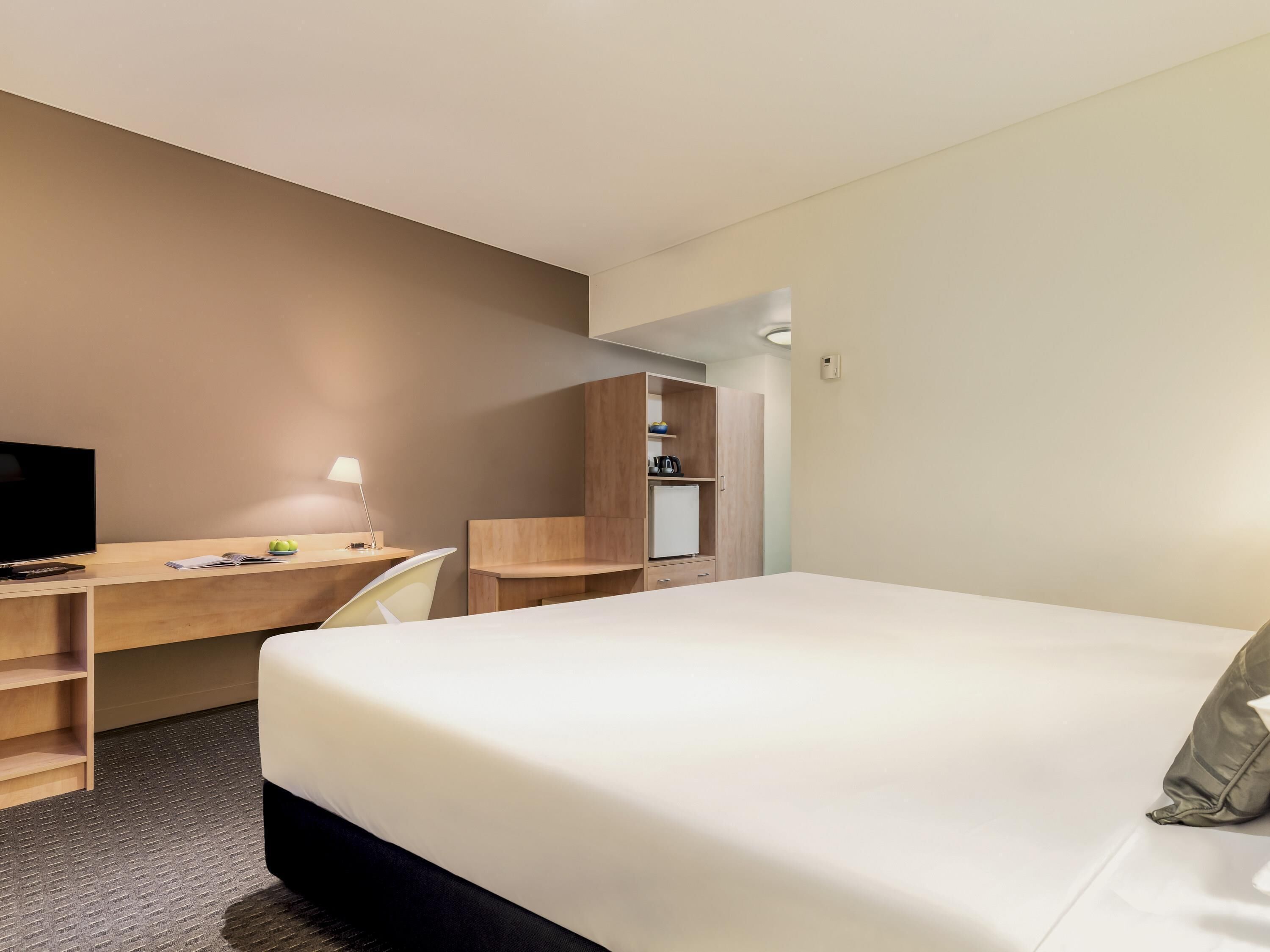 Una habitación de hotel con cama, escritorio, silla y una pequeña kitchenette.