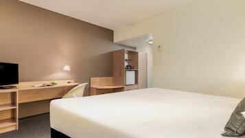 Una habitación de hotel con cama, escritorio, silla y una pequeña kitchenette.