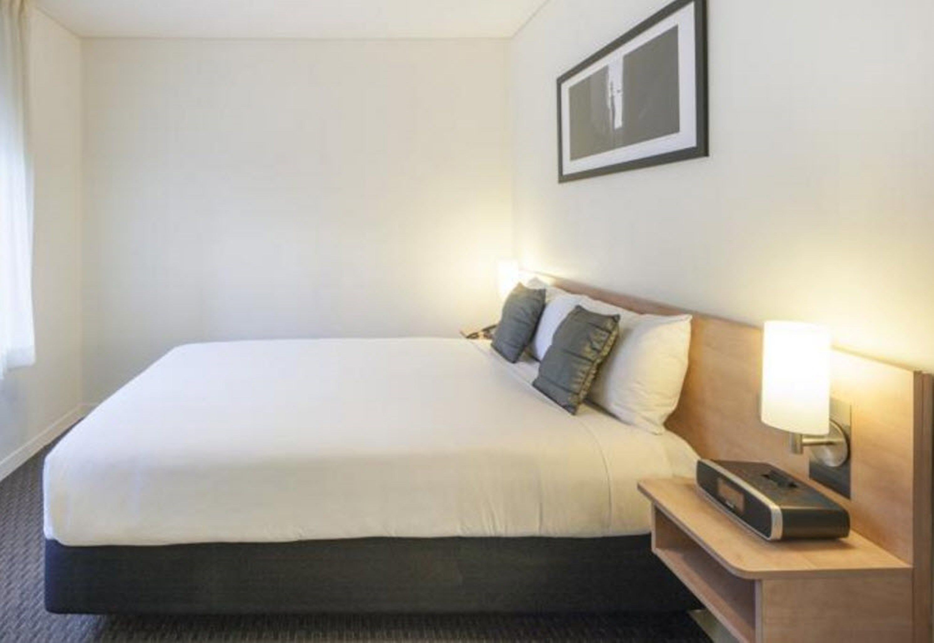 Una habitación de hotel con una cama grande, una mesita de noche con lámpara y un cuadro en la pared.