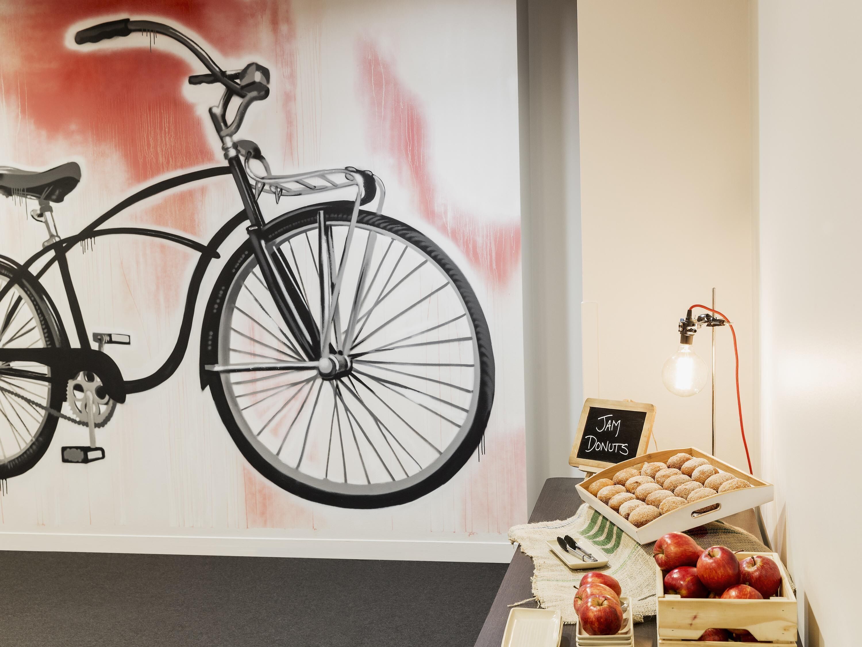 A wall-mounted bicycle, a tray of donuts, a sign reading 'JAM DONUTS', and a light bulb on a stand.