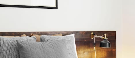 A neatly made bed with grey pillows, a framed picture above it, and a bedside lamp.