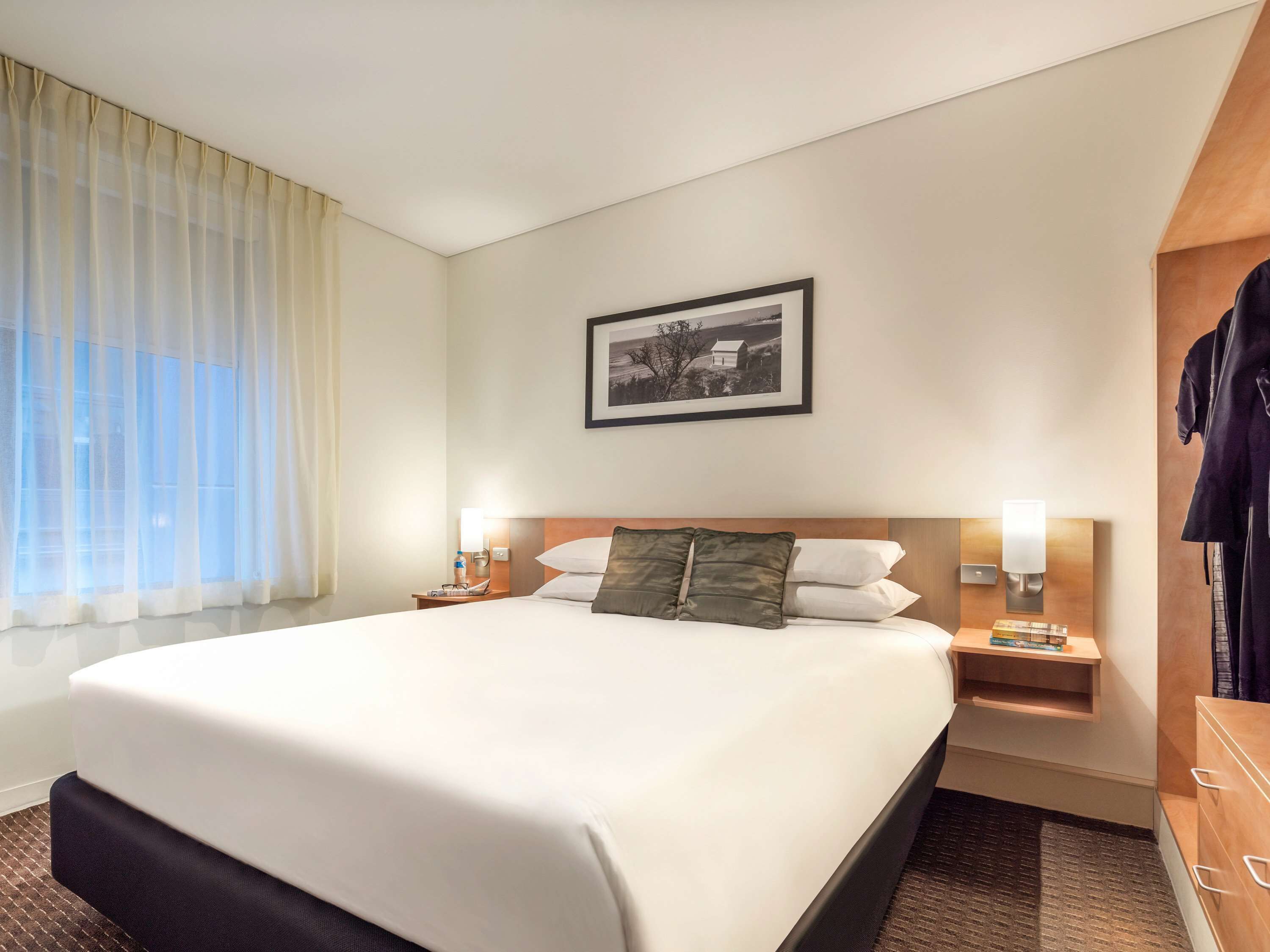 A hotel room with a large bed, a nightstand with a lamp, a wardrobe, and a framed picture on the wall.