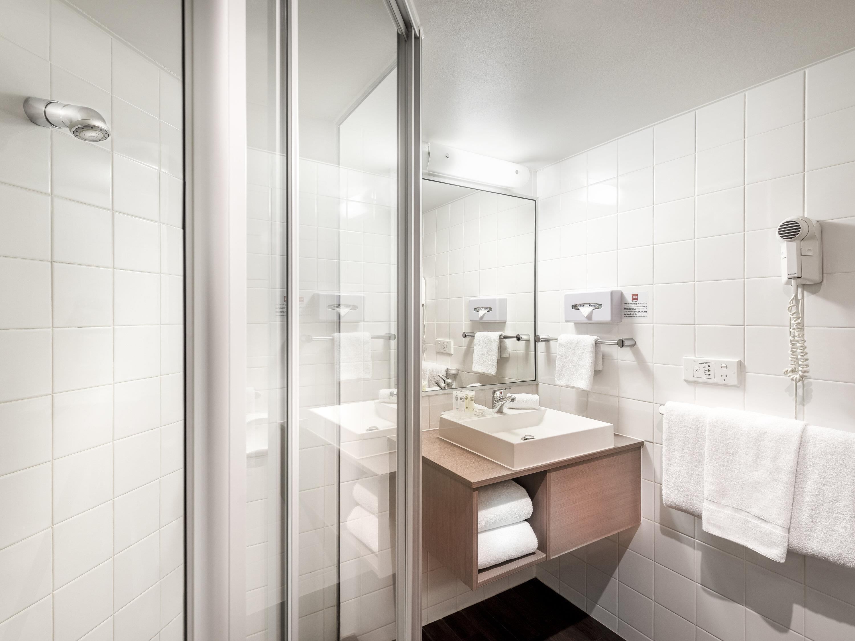 Un baño moderno con cabina de ducha de vidrio, un lavamanos con espejo y un secador de pelo montado en la pared.