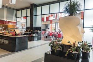 A modern restaurant with a central counter, red chairs, and potted plants.