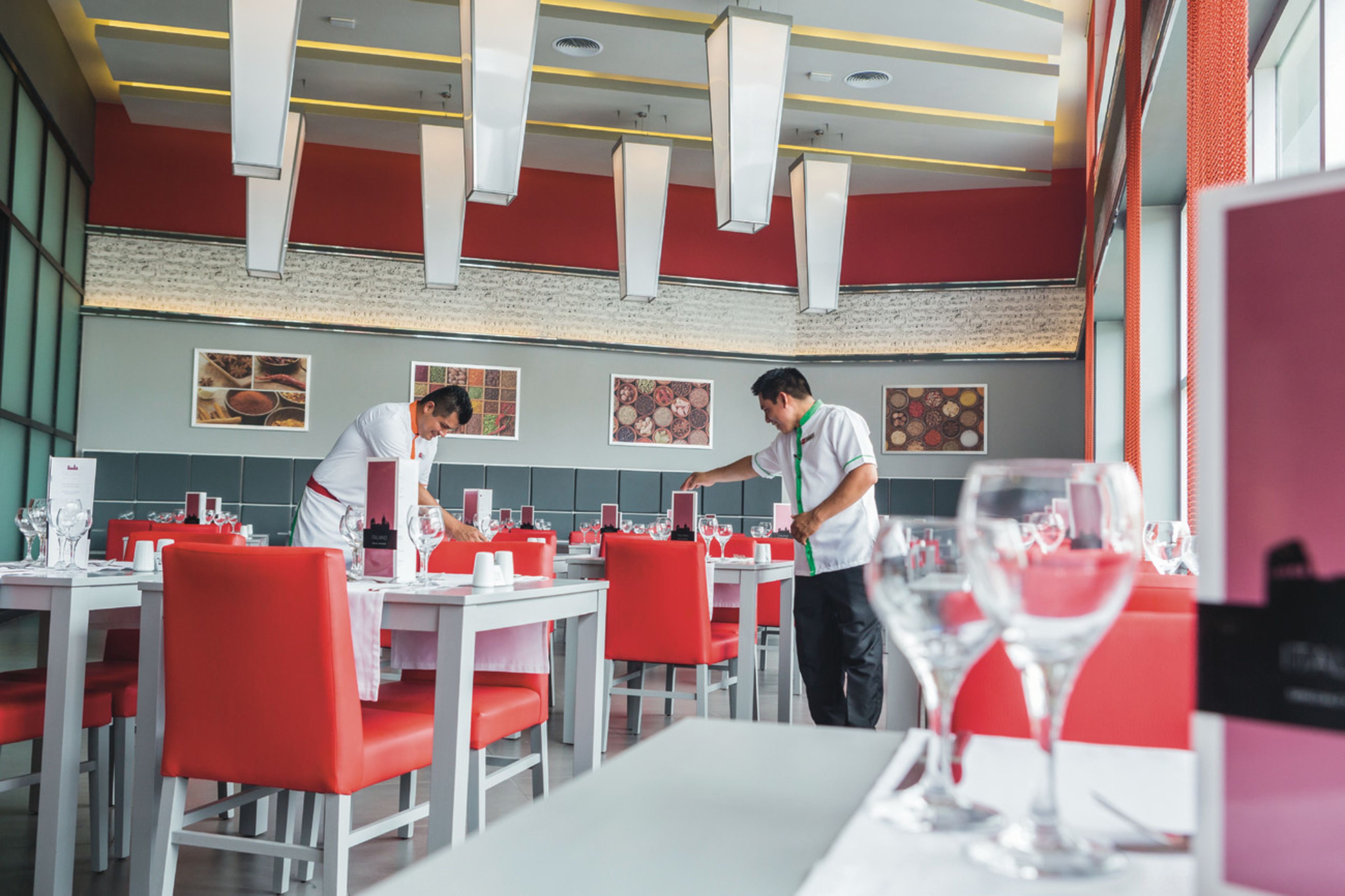 L’intérieur d’un restaurant avec des chaises rouges, des tables blanches et un mur en briques.