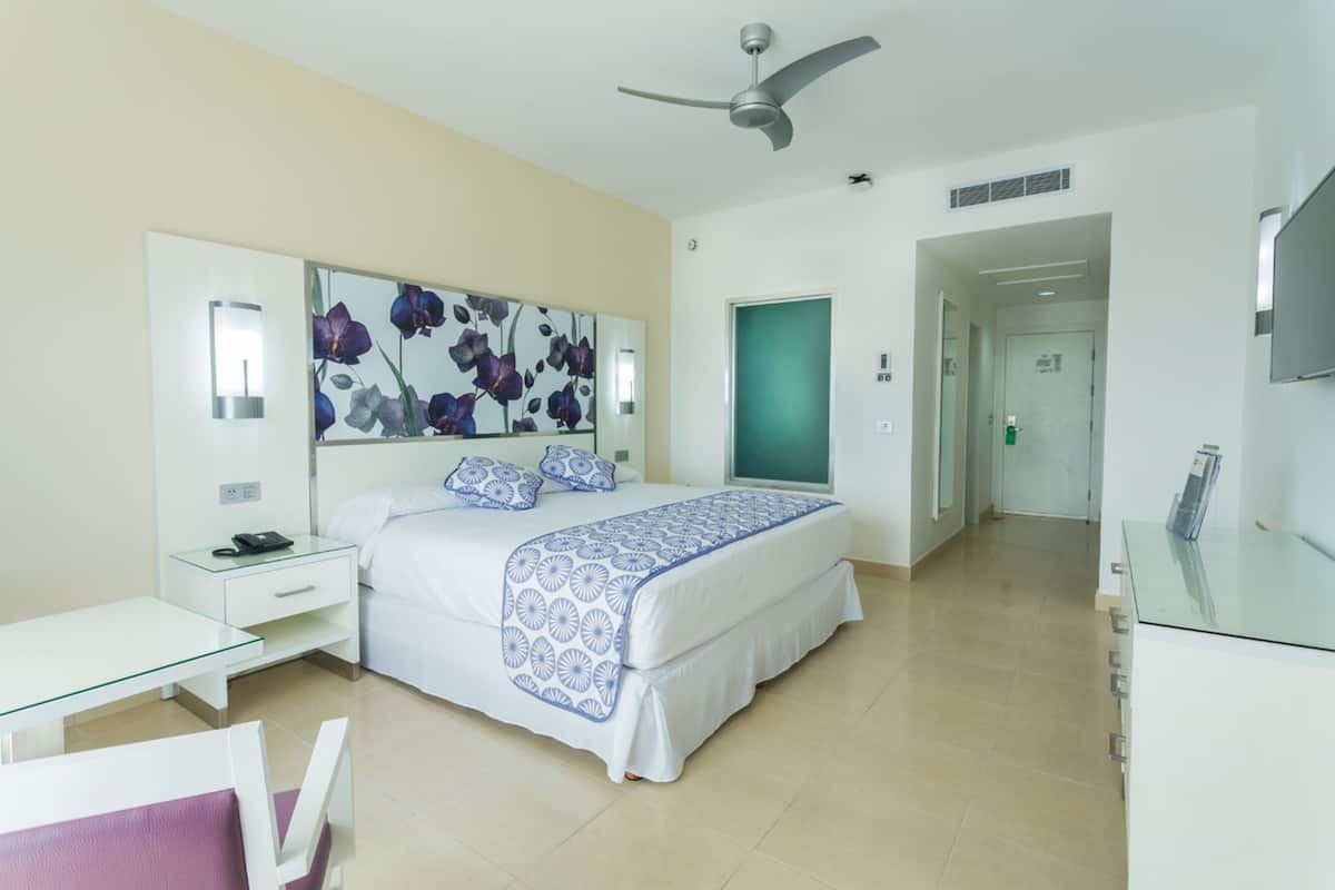 Habitación de hotel con cama, mesita de noche y un espejo grande con diseño floral.