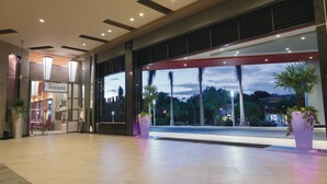 Un hall d’hôtel moderne avec une grande façade vitrée, un restaurant Traciata et des plantes en pot.