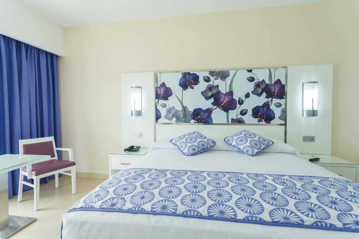 Habitación de hotel con cama, escritorio, silla y un espejo grande con diseño floral.