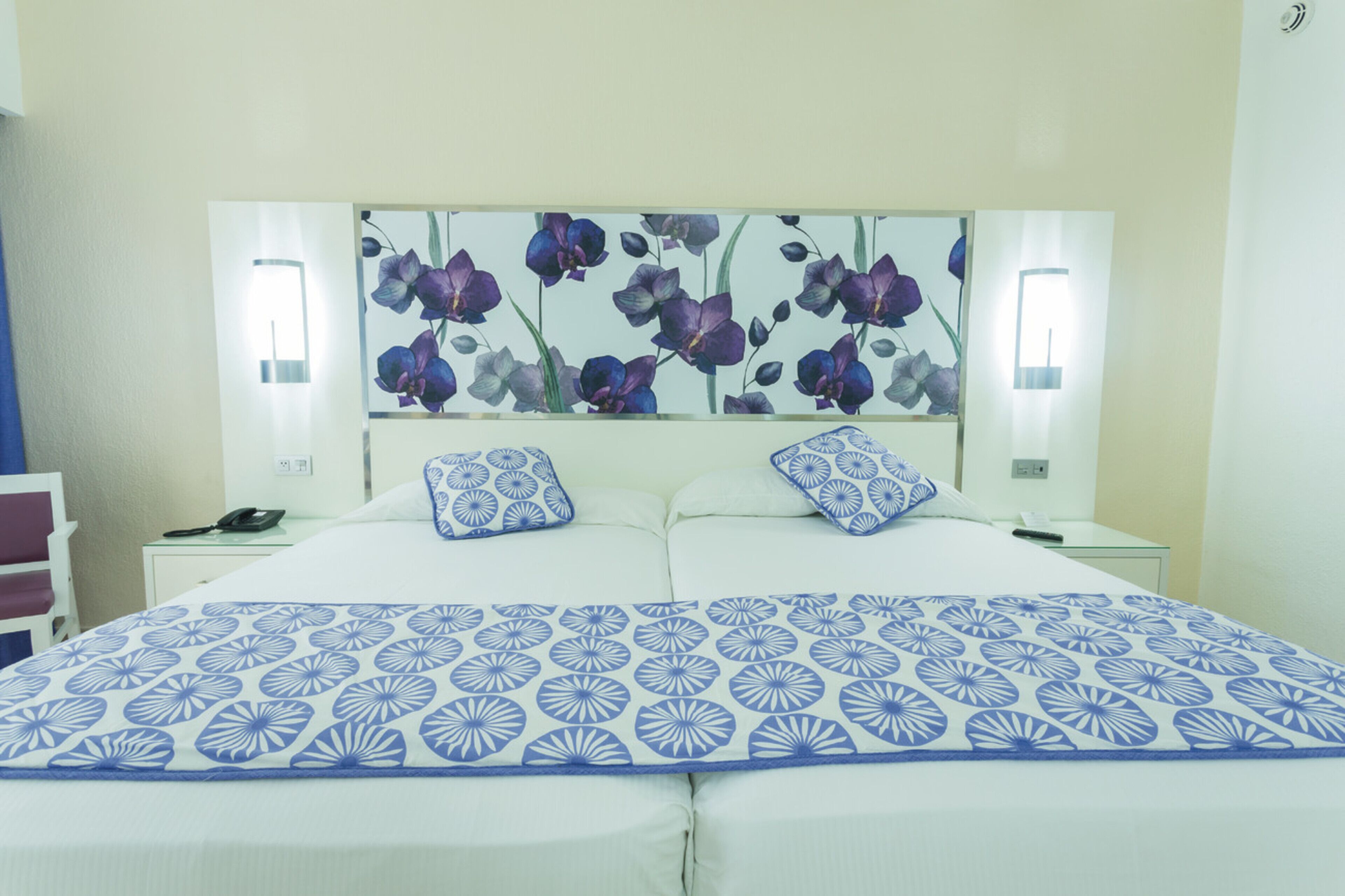 Een hotelkamer met een groot bed, twee nachtkastjes, een wandlamp en een hoofdbord met bloemenprint.