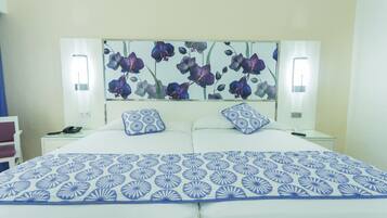 Habitación de hotel con una cama grande, dos mesitas de noche, una lámpara de pared y un cabecero estampado con motivos florales.