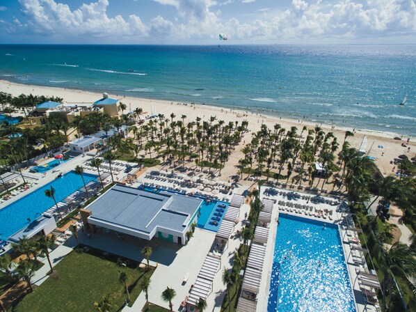 Relax by the resort's two pools surrounded by sun loungers and palm trees, with a scenic ocean view.