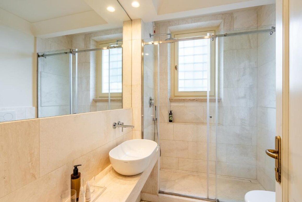 A modern bathroom with a large mirror, a white sink, and a glass-enclosed shower.