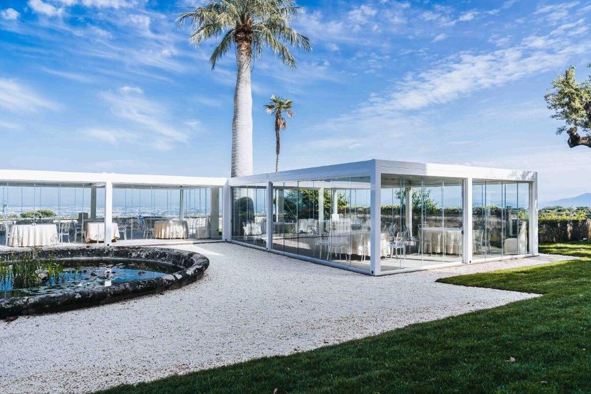 A modern outdoor dining area with glass walls, a palm tree, and a small pond.