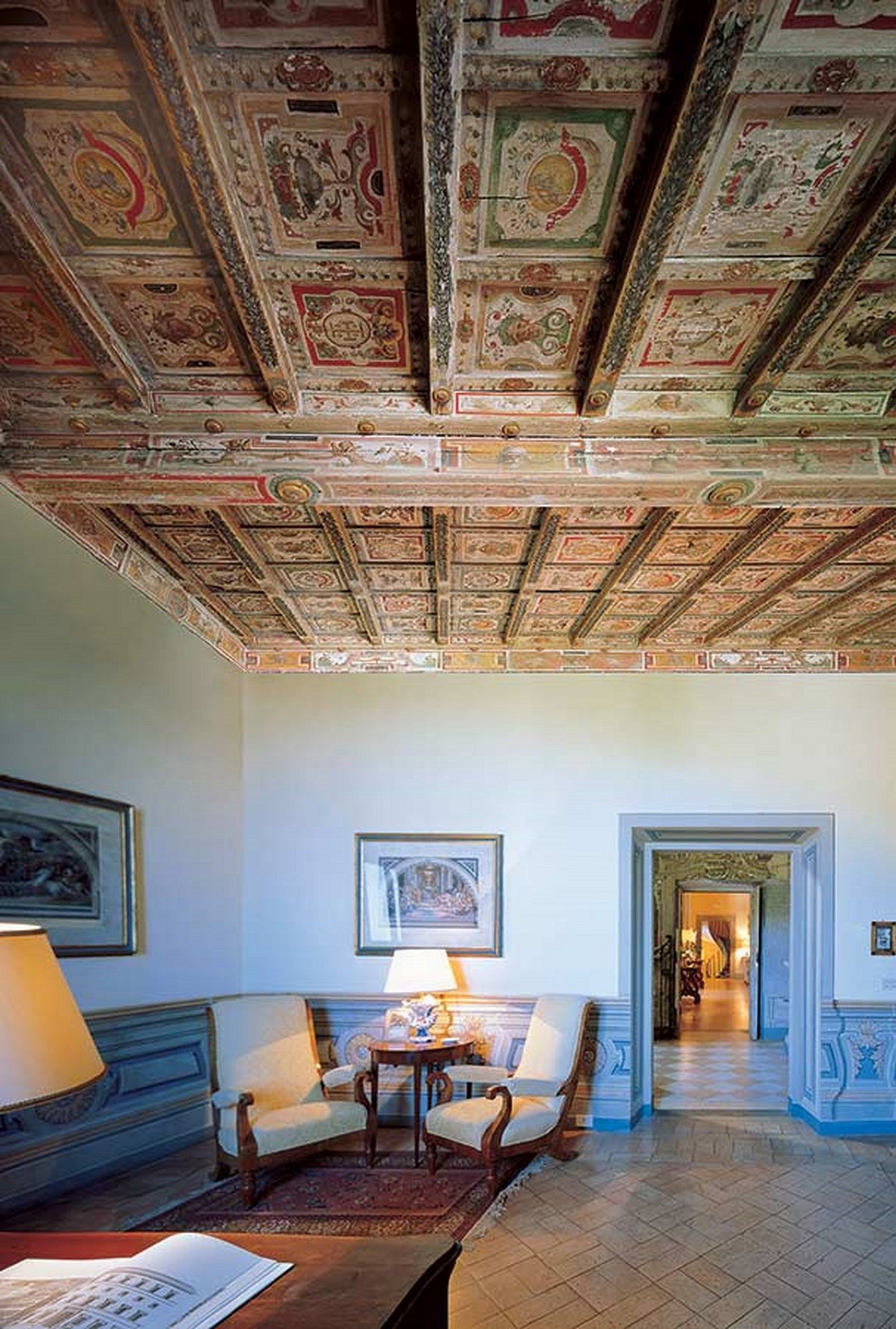 A room with ornate ceiling frescoes, a chandelier, and a view of a hallway.