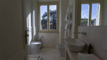 Een moderne badkamer met toilet, wastafel en douche. Een raam zorgt voor daglicht en uitzicht op bomen.