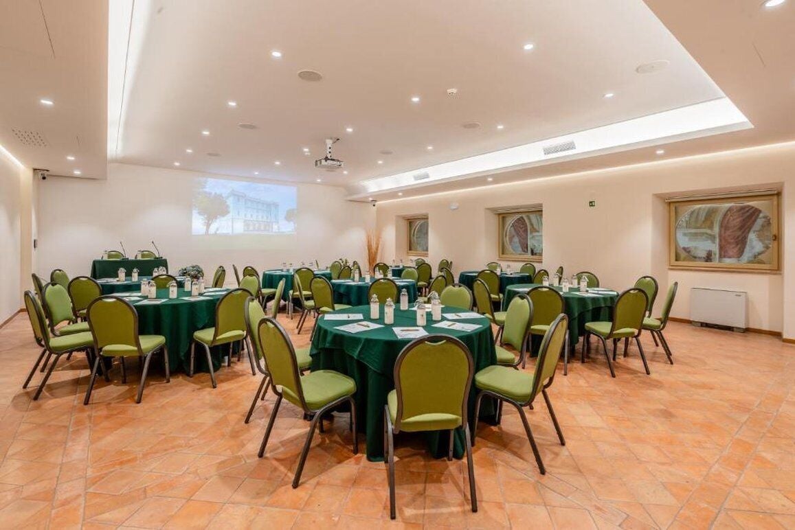 Une salle de conférence dotée de plusieurs tables et chaises, ainsi que de projecteurs et d’écrans.