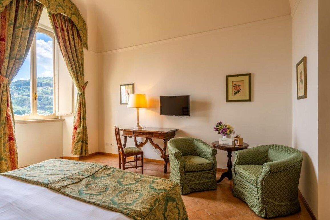 Habitación de hotel con una cama, dos sillones, un escritorio con lámpara, televisión y cuadros en la pared.
