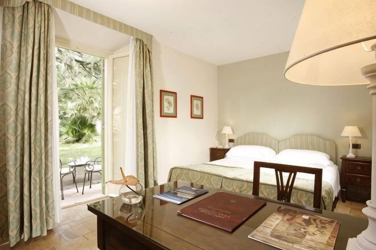 Een hotelkamer met een bed, een bureau met stoel, een lamp en uitzicht op het buitenland.