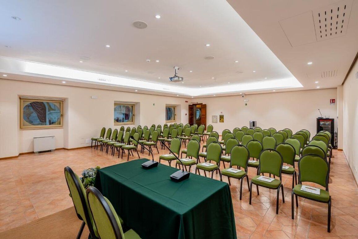 Una sala conferenze con file di sedie, un proiettore e un tavolo con cartellini.