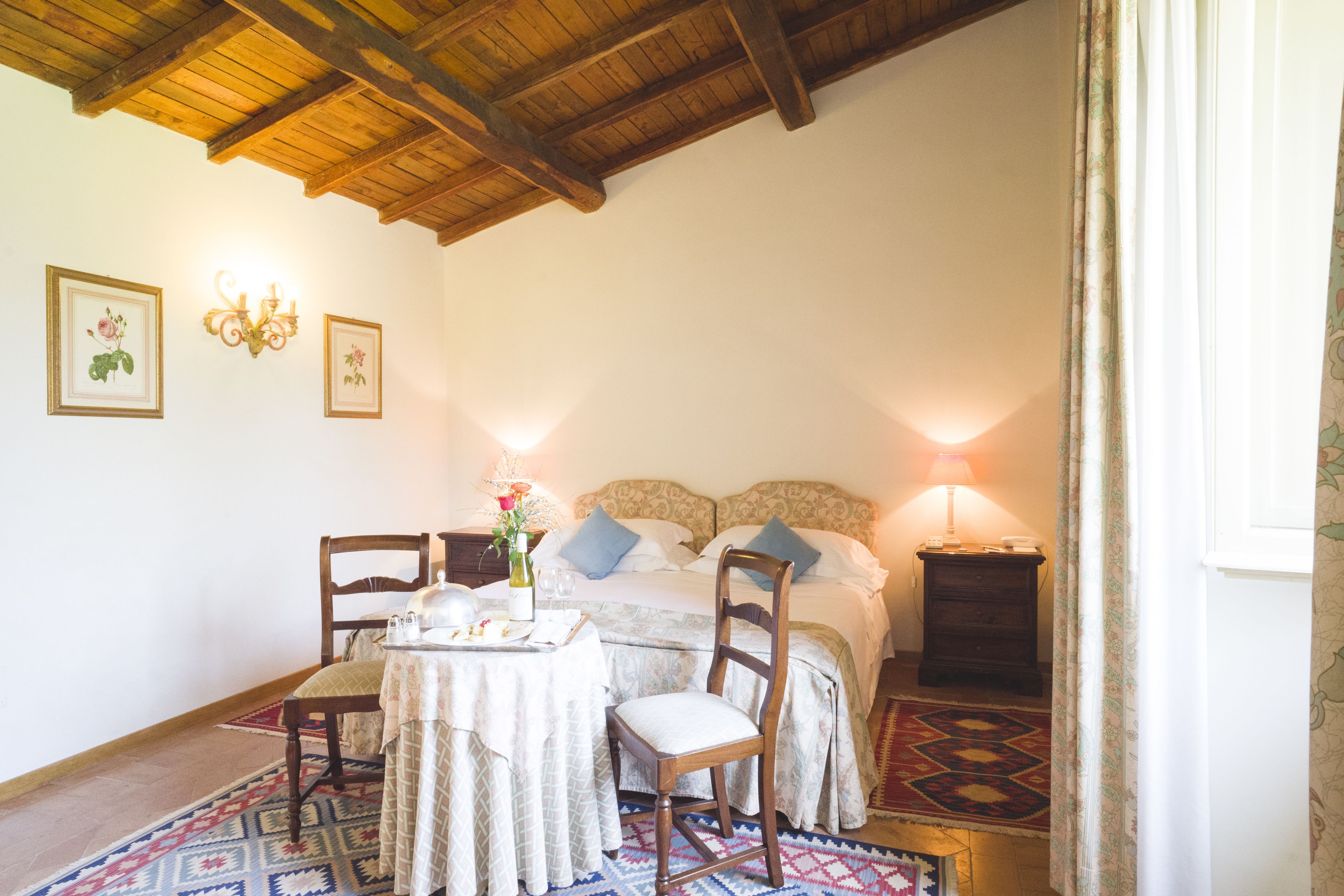 Una camera da letto con soffitto in legno, un letto con cuscini, un comodino con una lampada e una sedia.