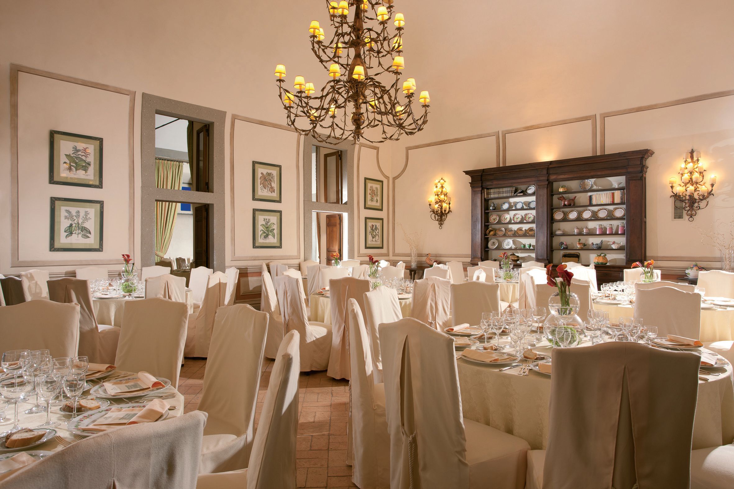 A formal dining room with multiple round tables, chairs, and a chandelier.