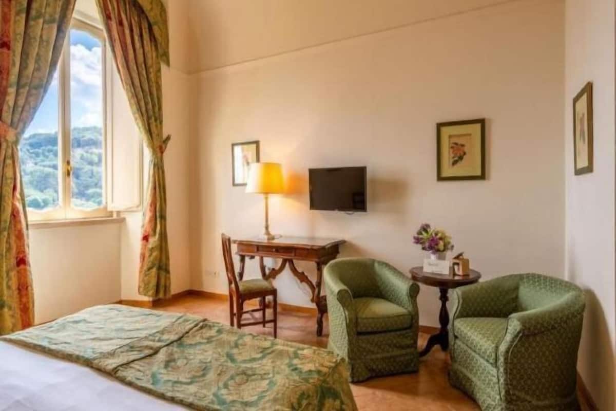 Een hotelkamer met een bed, twee fauteuils, een bureau met lamp, een televisie en lijstjes met foto's aan de muur.