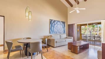 A modern living room with a round table, grey chairs, a sofa, and a wooden coffee table. There is a ceiling fan and a large abstract painting on the wall.