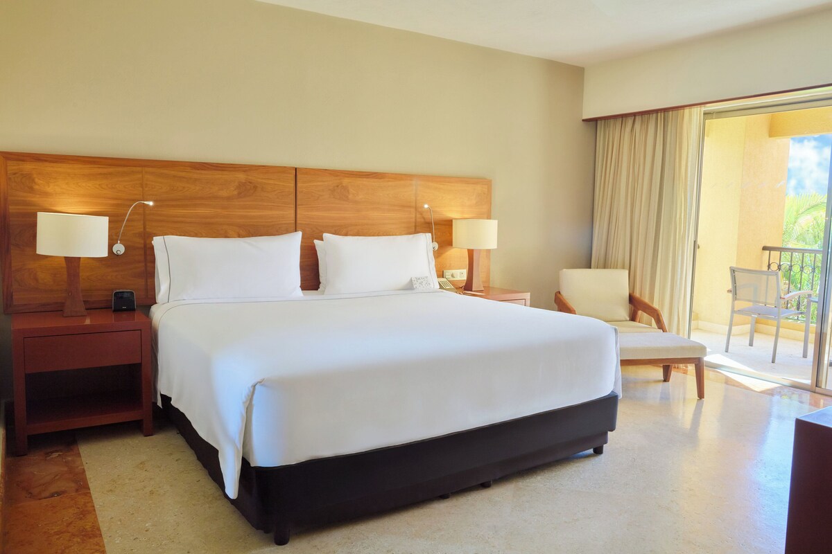 A hotel room with a large bed, two bedside tables with lamps, a chair, and a balcony with a view.