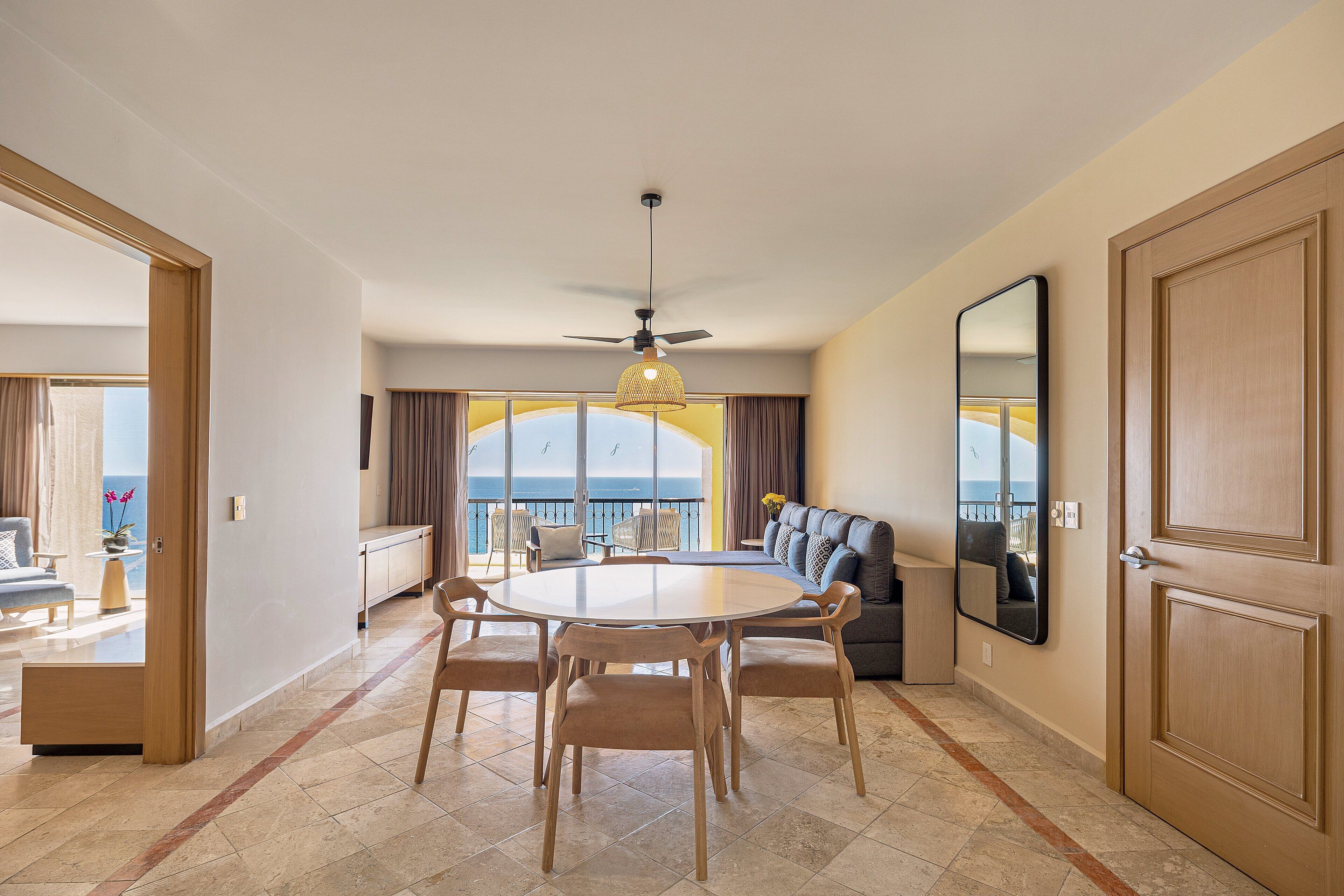 A spacious living area with a round dining table, comfortable seating, a ceiling fan, and a large window offering a view of the outdoors.