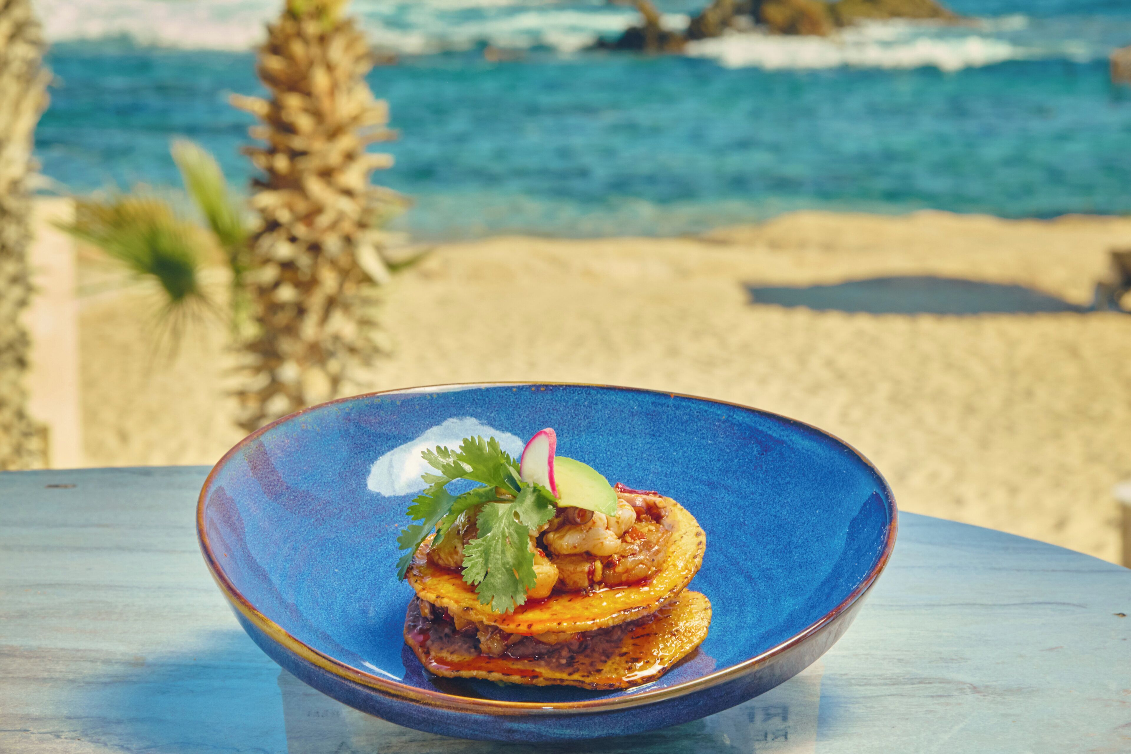 A blue bowl with a dish on a table by the beach.
