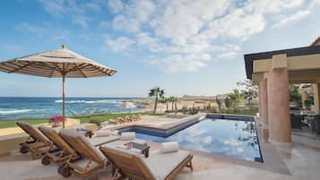 Zona de piscina con sillones de descanso y una sombrilla, con vistas al océano.