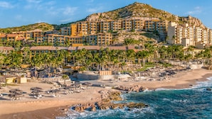 Un hôtel situé sur la côte, composé de plusieurs bâtiments, avec une plage et des palmiers.
