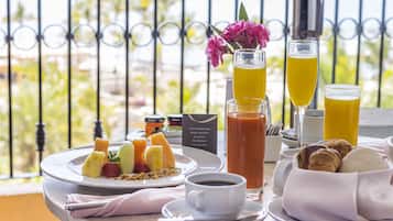 A breakfast setting with a variety of fruits, pastries, and beverages on a balcony overlooking a scenic view.