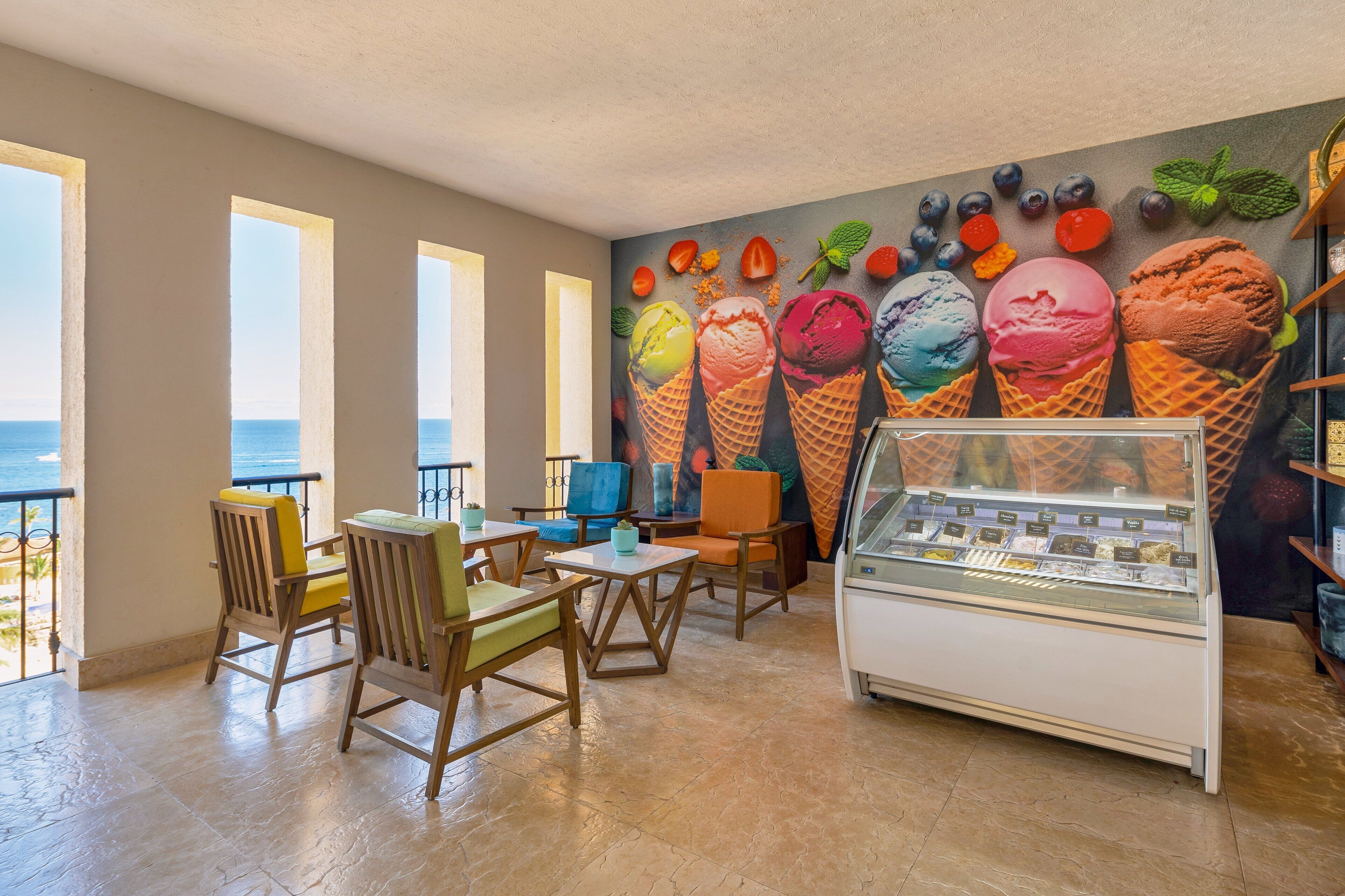 Un restaurante con un mural de conos de helado, sillas de madera y una vitrina de postres.