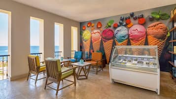 Un restaurante con un mural de conos de helado, sillas de madera y una vitrina de postres.