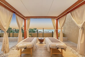 Una habitación con dos camillas de masaje, suelo de madera y vista al mar.