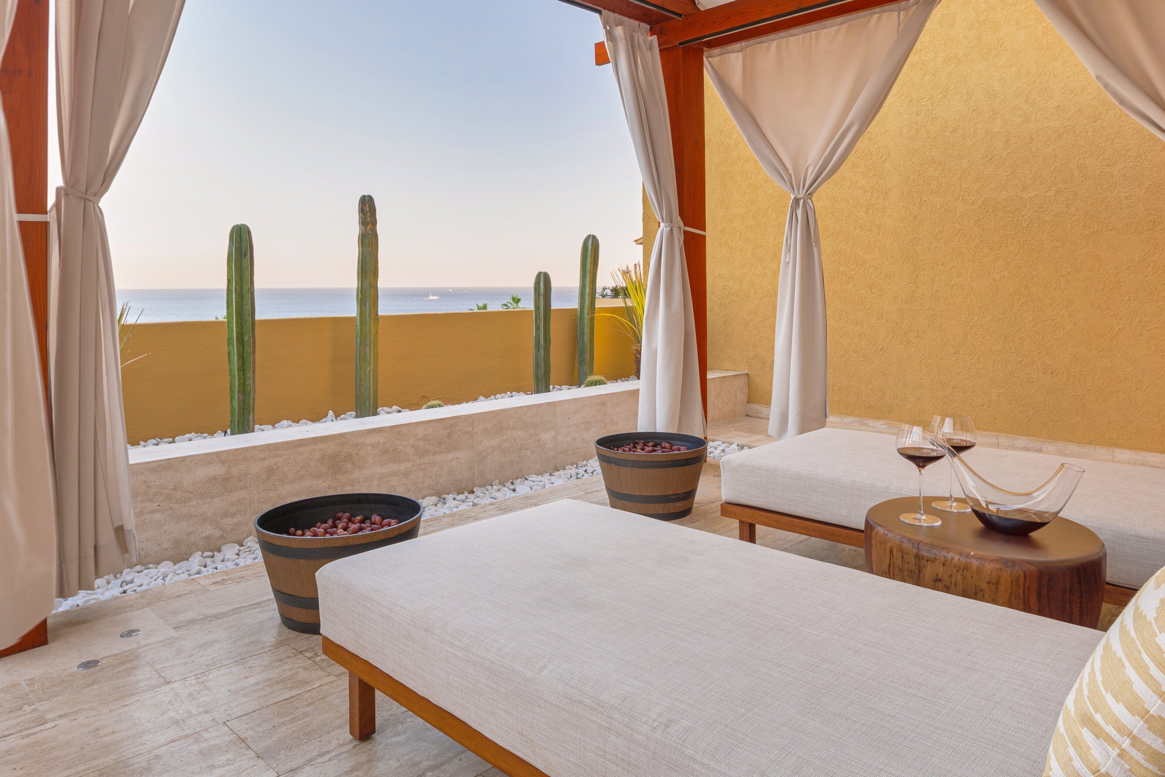 Habitación con vistas a la playa, que incluye dos camas, una mesa de madera con copas de vino y un recipiente grande de bayas rojas.