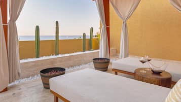 Habitación con vistas a la playa, que incluye dos camas, una mesa de madera con copas de vino y un recipiente grande de bayas rojas.