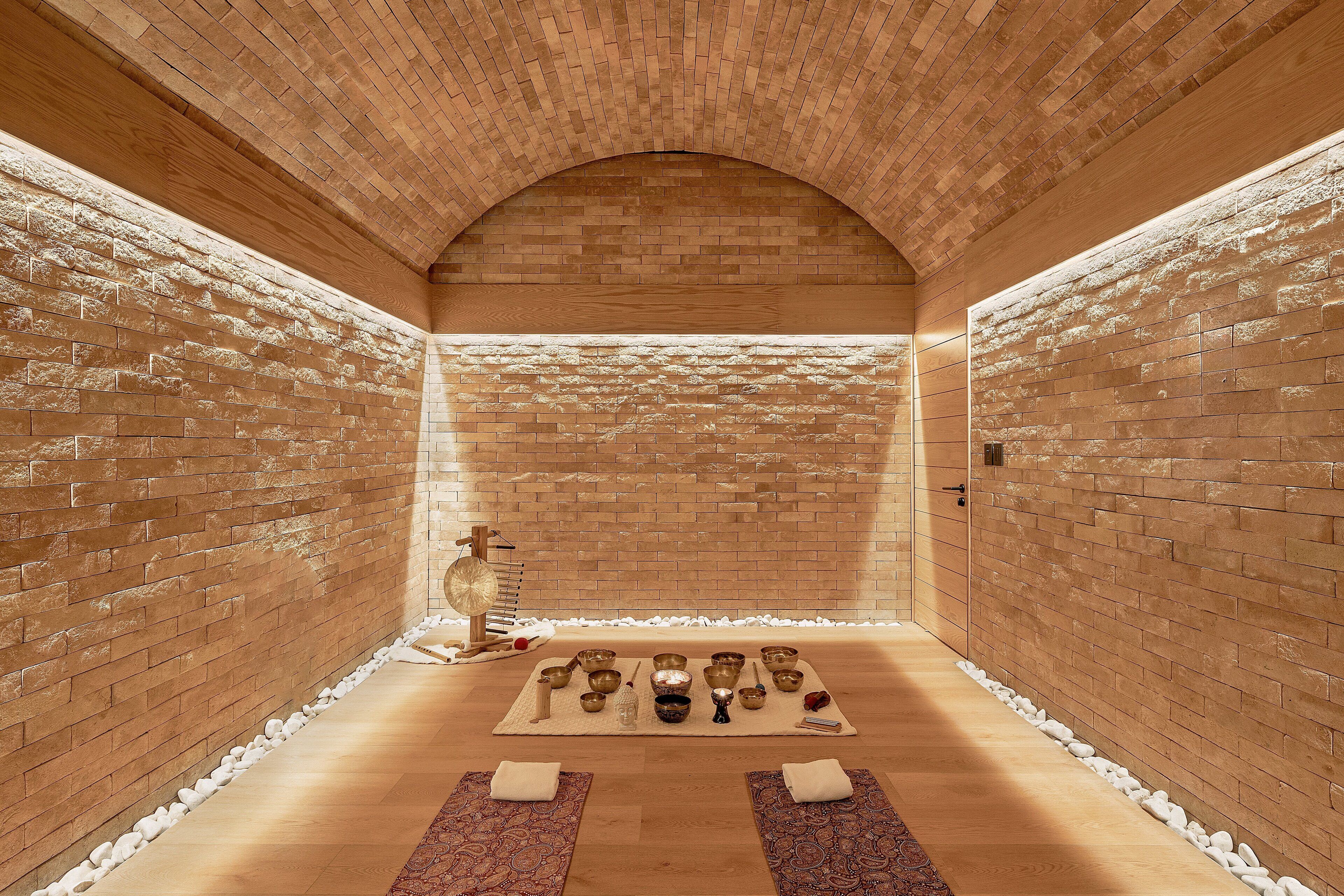 Une salle de spa avec un mur en briques, un plancher en bois et une série de bols et de pierres disposés sur un tapis.